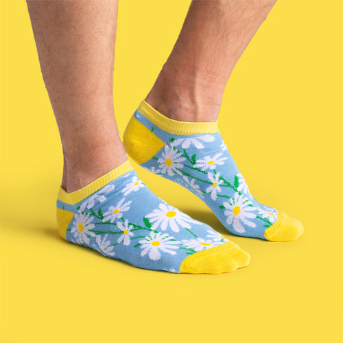 Ljusblå sneakersstrumpor med prästkragemönster på fötter mot en gul bakgrund - Svenskhusman.