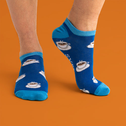 Blå sneakersstrumpor med mönster av kaffekoppar på en person mot en orange bakgrund, Svenskhusman.