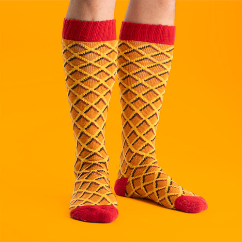 Kexchokladmönstrade skidsockor i gult och rött från Svenskhusman burna mot en orange bakgrund.