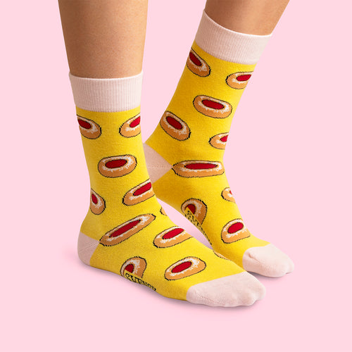 Yellow socks with raspberry cave cookie patterns by Svenskhusman on feet against a pink background.