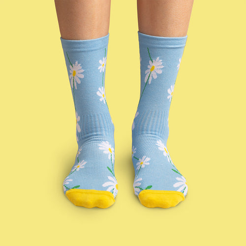 Blue Svenskhusman compression socks with a white daisy pattern and yellow toes against a yellow backdrop.