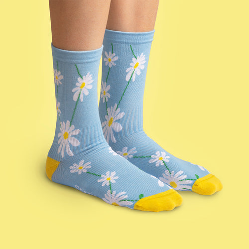 Light blue compression socks featuring white daisies and yellow accents on a person with a yellow backdrop.