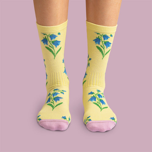 Yellow compression socks with bluebells and pink toes by Svenskhusman against a purple background.