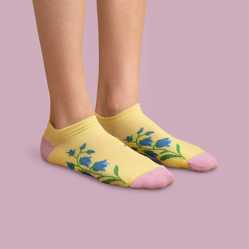 Gula sneakers-stödstrumpor med mönster av blåklockor och rosa detaljer på fötter från Svenskhusman.