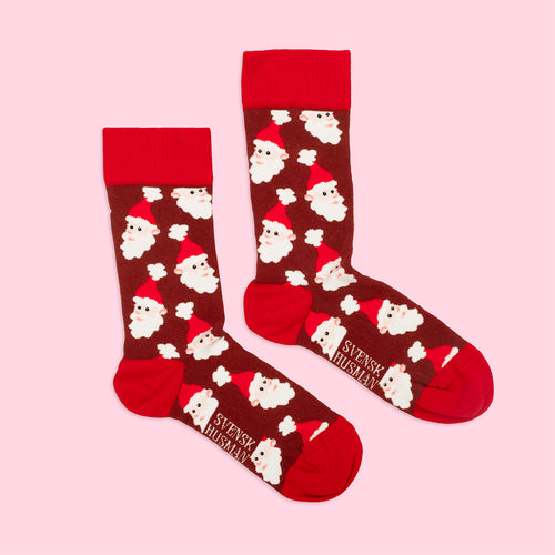Brown Christmas socks with a Santa face pattern and red details from Svenskhusman on a pink background.