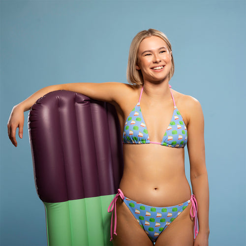 Blå trekantsbikini med mönstret Prinsesstårtan från Svenskhusman på en modell vid en badmadrass.