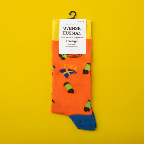 Orangea strumpor med mönster av dammsugare, svenska flaggor och texten fika från Svenskhusman.