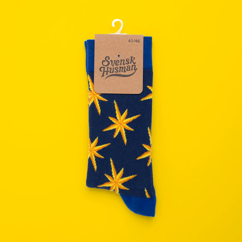 Dark blue Svenskhusman socks with yellow poinsettia patterns displayed on a bright yellow background.