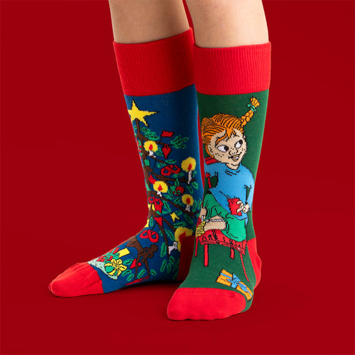 Barnstrumpor i blått och grönt med motiv från Pippi Räddar Julen mot röd bakgrund, Svenskhusman.