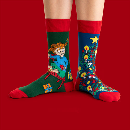 Julstrumpor i grönt och blått med Pippi Långstrump och en klädd julgran på fötter mot röd bakgrund.