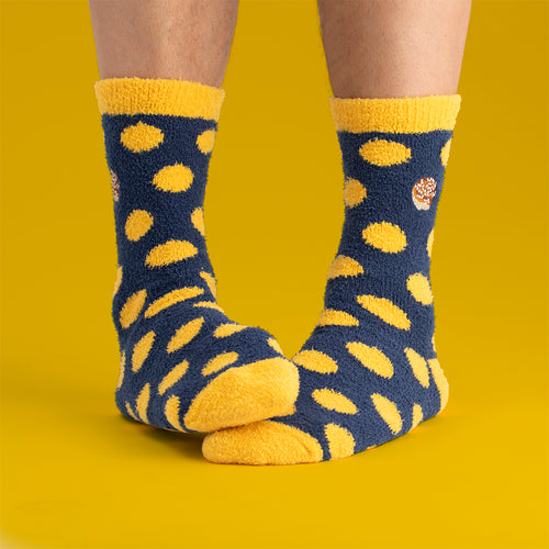 Fluffy blue socks with yellow dots and cinnamon bun pattern by Svenskhusman on a yellow background.