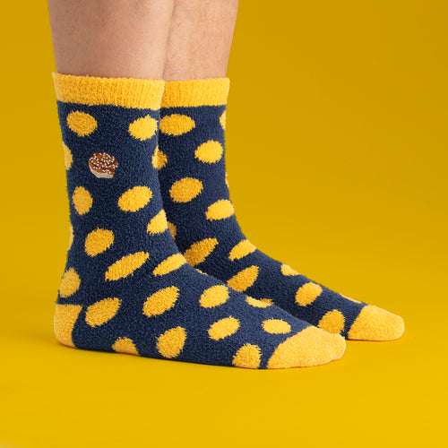 Fluffy blue cinnamon bun socks with yellow dots by Svenskhusman, worn against a bright yellow background.