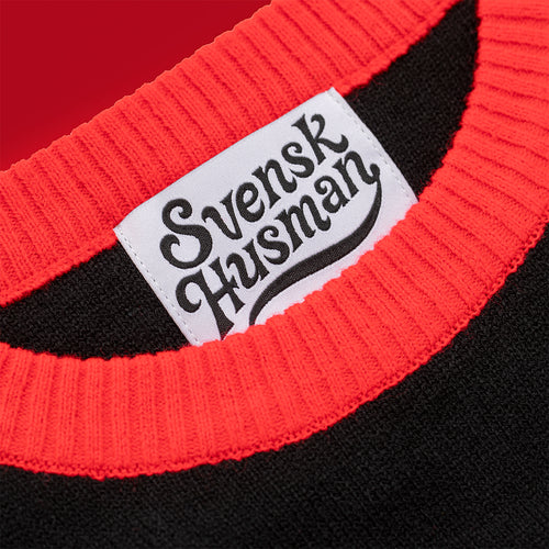 Svenskhusman label inside the neckline of a black knitted Christmas sweater with a red ribbed collar.
