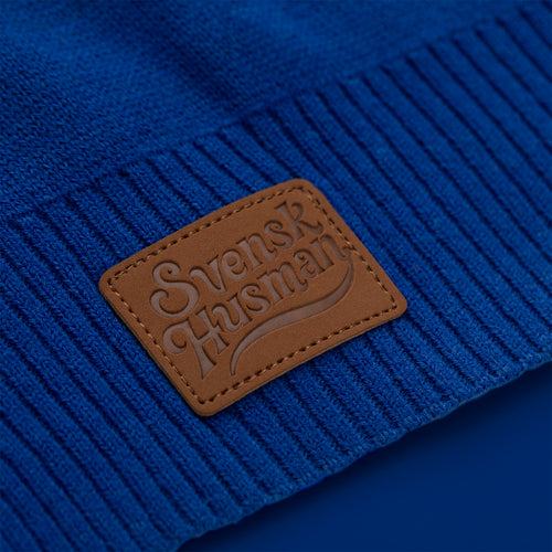 Brown faux leather logo on a blue knitted Christmas sweater with saffron bun motifs from Svenskhusman.