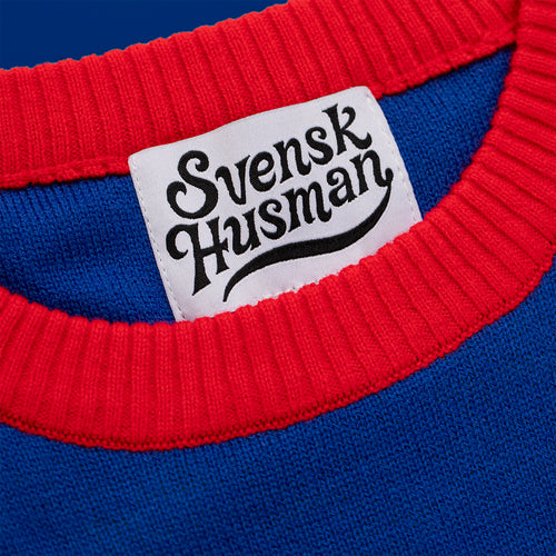 Blauer gestrickter Weihnachtspullover mit rotem Rippkragen und weißem Logo-Etikett von Svenskhusman.