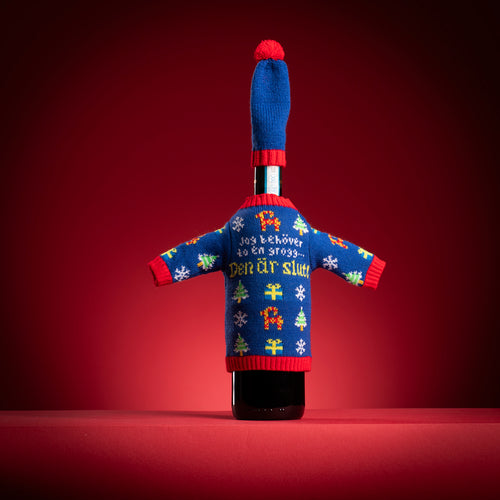 Blå stickad flasktröja med texten Jag behöver en grogg och matchande hatt på en flaska - Svenskhusman