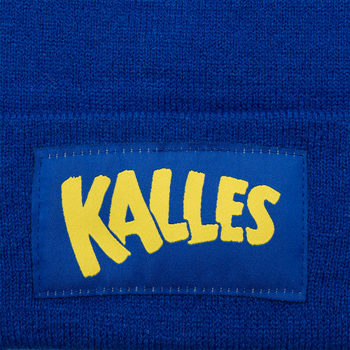 Stickad blå mössa försedd med den ikoniska gula Kalles Kaviar-logotypen från Svenskhusman i närbild.