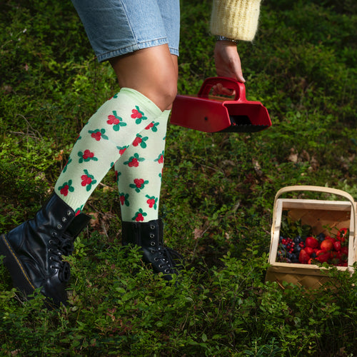 Ljusgröna stödstrumpor med lingonmönster från Svenskhusman i en skog med bärplockare.