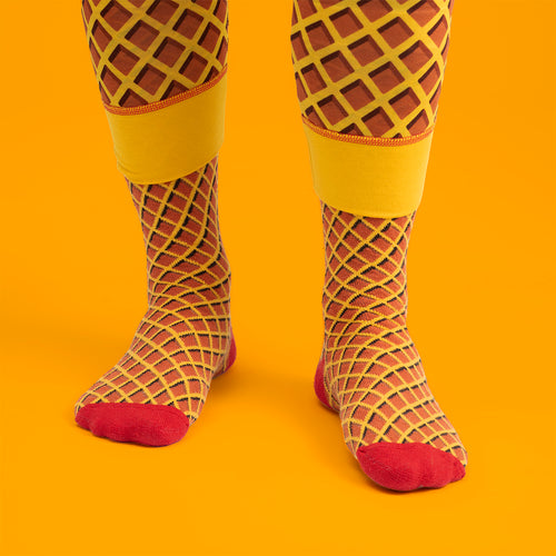 Gula skidsockor med Kexchoklad-mönster och röda detaljer från Svenskhusman bärs mot en gul bakgrund.