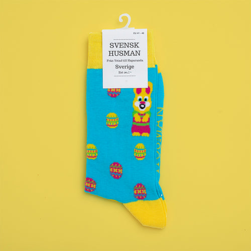 Light blue Svenskhusman socks with yellow Easter bunnies and eggs pattern on a yellow background.