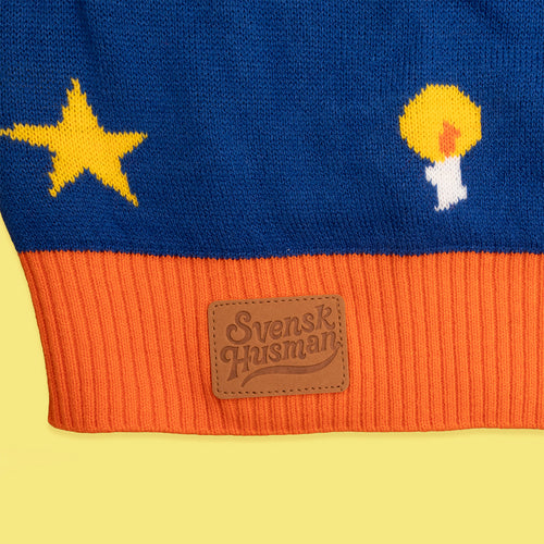 Blå stickad jultröja med mönster av stjärna och ljus, orange mudd och läderlogotyp från Svenskhusman.