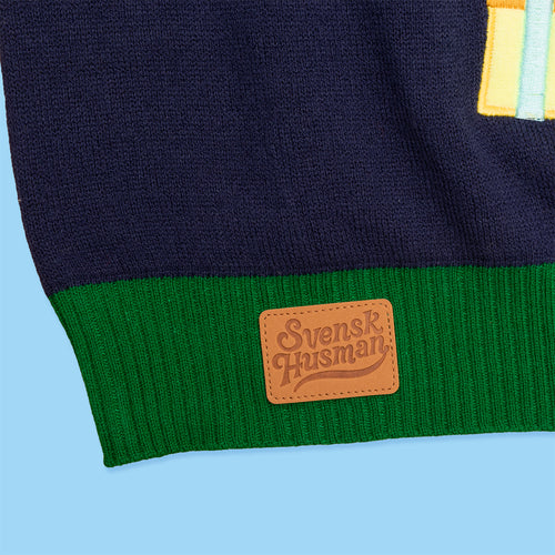 Mörkblå stickad jultröja med grön mudd och Svenskhusmans logotyp på en brun läderlapp.