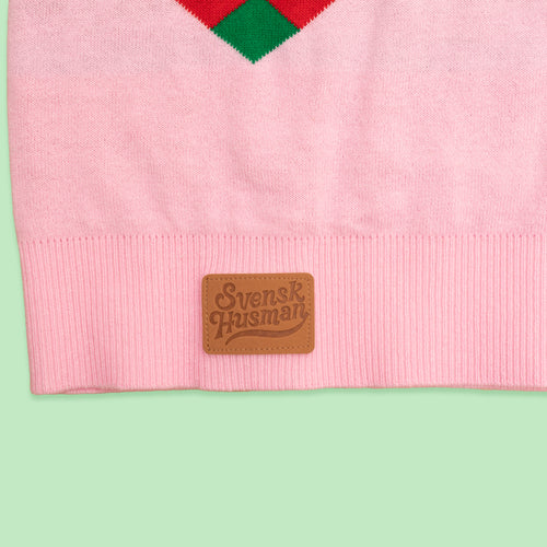 Närbild på rosa stickad jultröja i bomull med Schwedischhusman-logotyp på en läderpatch vid nederkanten.