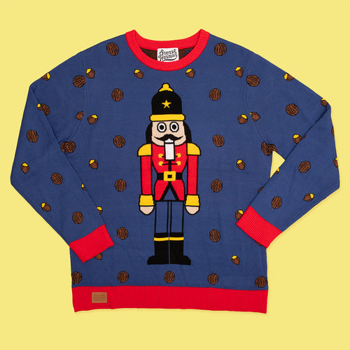 Blå stickad jultröja med nötknäpparmotiv och röda detaljer från Svenskhusman på gul bakgrund.