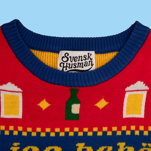 Röd stickad jultröja med julöl-motiv och blå krage med Svenskhusman-etikett i nacken.
