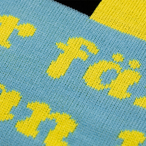 Närbild på den stickade gula texten mot blå bakgrund på julvästen Sån där färg från Svenskhusman.