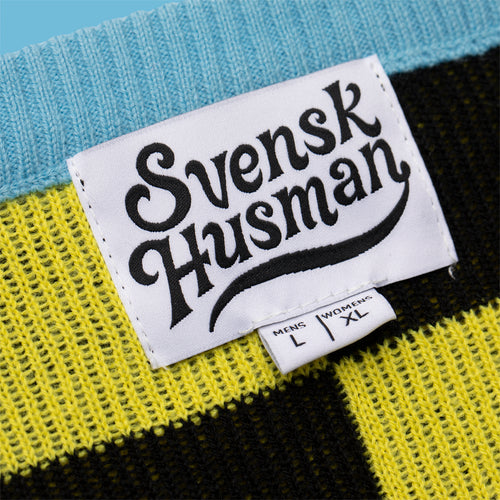 Närbild på Svenskhusman-etikett på en stickad jultröja i gult och svart med blå krage.