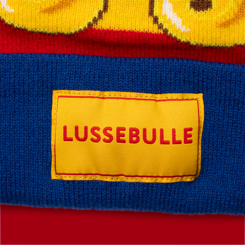 Stickad blå mössa med en gul etikett och texten Lussebulle - Svenskhusman