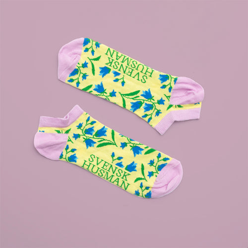 Gula sneakersstrumpor med blåklockor och rosa detaljer på lila bakgrund från Svenskhusman.