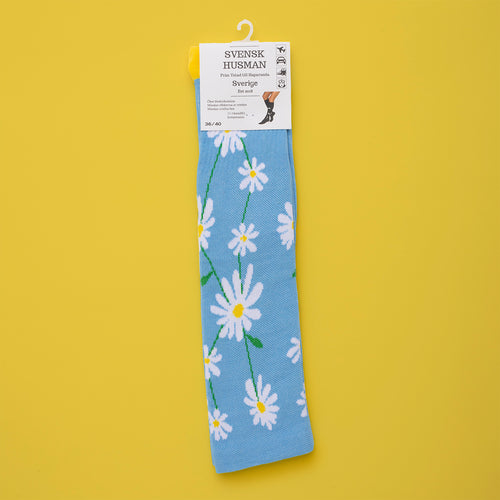 Light blue support stockings with white daisy patterns by Svenskhusman on a yellow background.