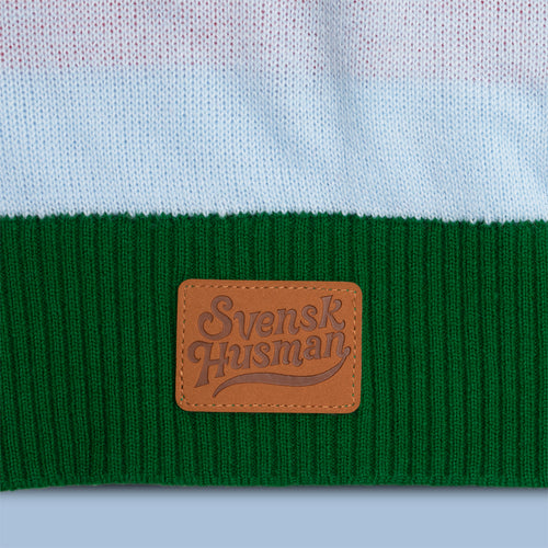 Detail of a gingerbread house Christmas sweater featuring a green knitted cuff and brown leather Svenskhusman label.