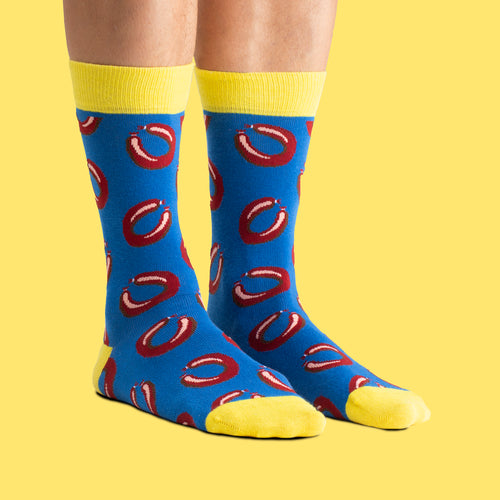 Blue and yellow Svenskhusman socks with a Falukorv pattern, worn against a bright yellow background.