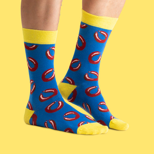 Blue and yellow socks with a falukorv pattern from Svenskhusman, shown on feet against a yellow background.