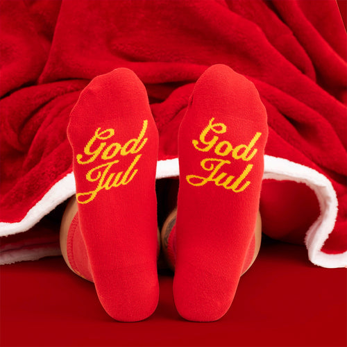 Röda julstrumpor med texten God Jul i gult på undersidan, instoppade under en röd filt från Svenskhusman.