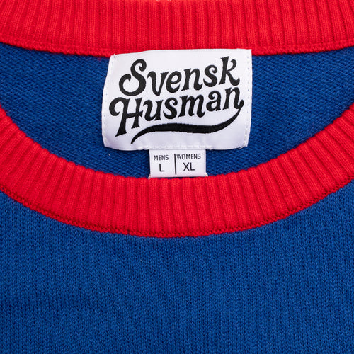 Svenskhusman neck label and size tag on a blue knitted Christmas sweater with a red ribbed collar.