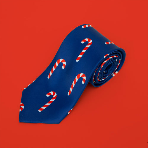 Blå slips i polyester prydd med festliga polkagrisar, rullad mot röd bakgrund från Svenskhusman.
