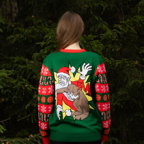 Grön jultröja Tomtejävel för dam med kaxigt motiv, sedd bakifrån i en stämningsfull granskog.