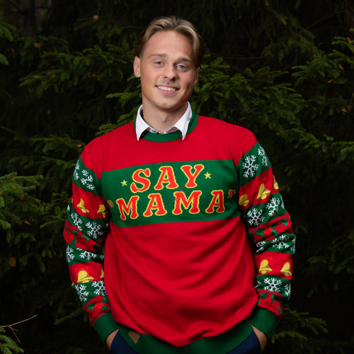Gestrickter Herren-Weihnachtspullover in Rot und Grün mit „SAY MAMA“ Text, getragen von einem Mann im Wald.