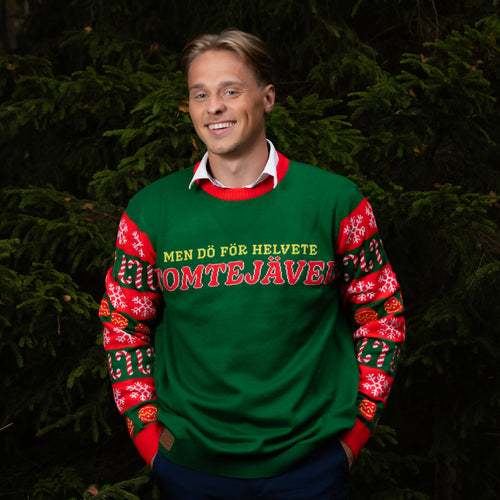 Grön jultröja med motivet Tomtejävel buren av en man i en julig granskog från Svenskhusman.