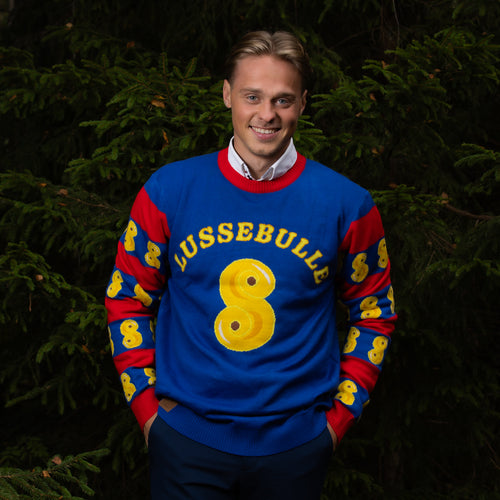 Blue saffron bun Christmas sweater from Svenskhusman worn by a smiling man in a spruce forest.