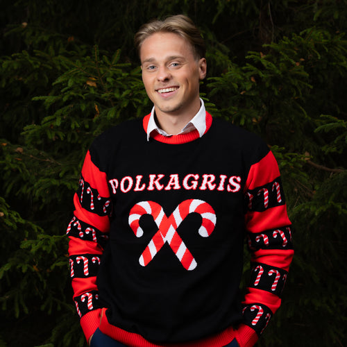 Black Svenskhusman Christmas sweater for men with red candy canes and Polkagris text, worn in front of a green tree.