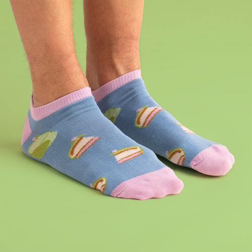 Ljusblå sneakersstrumpor med mönster av prinsesstårta och rosa detaljer från Svenskhusman mot grön bakgrund.