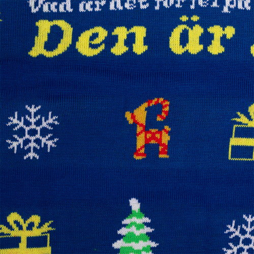 Blaue gestrickte Weihnachtsweste mit dem Text „Jag behöver ta en grogg“ und klassischen Festtagsmotiven.