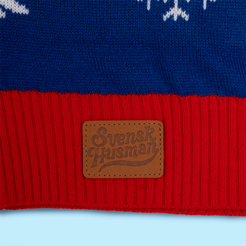 Svenskhusman leather logo patch on a red and blue knitted Christmas vest with white snowflake patterns.