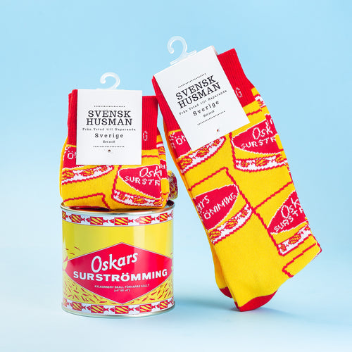 Rödgula bomullsstrumpor med Oskars Surströmming-motiv intill en konservburk från Svenskhusman.