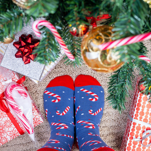Blaue Zuckerstangen-Socken mit roten Details unter einem Weihnachtsbaum mit Geschenken von Svenskhusman.
